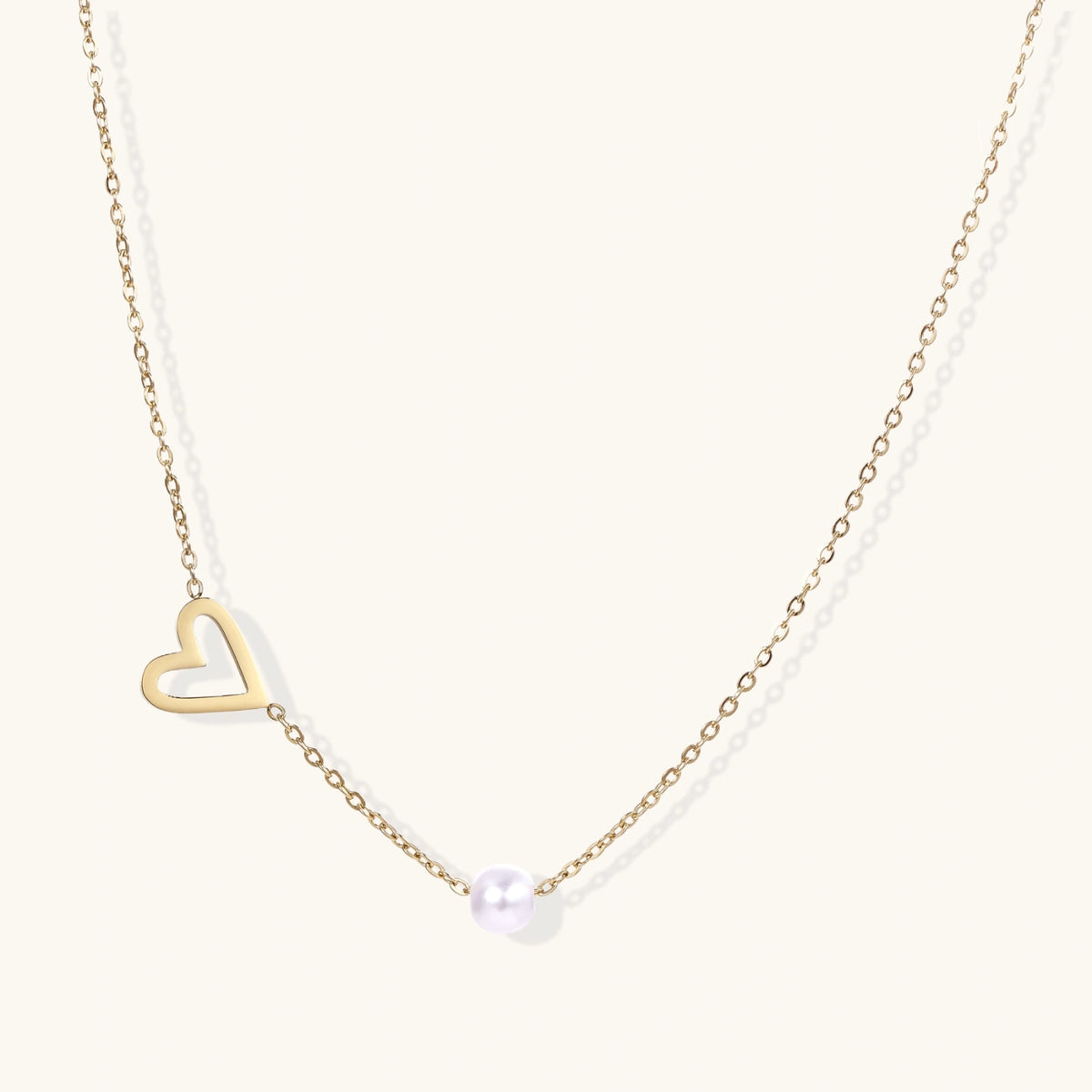 Dainty 14K gold plated stainless steel necklace with an open heart charm and a single round white bead on a cream background.