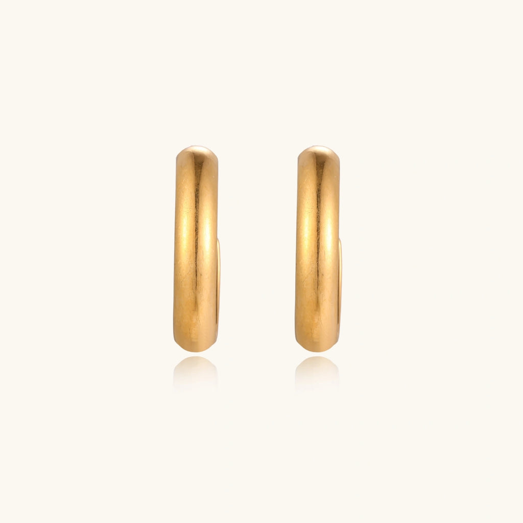 Chunky tubular hoop earrings in warm 14K gold-plated finish with smooth polished surface on cream background.